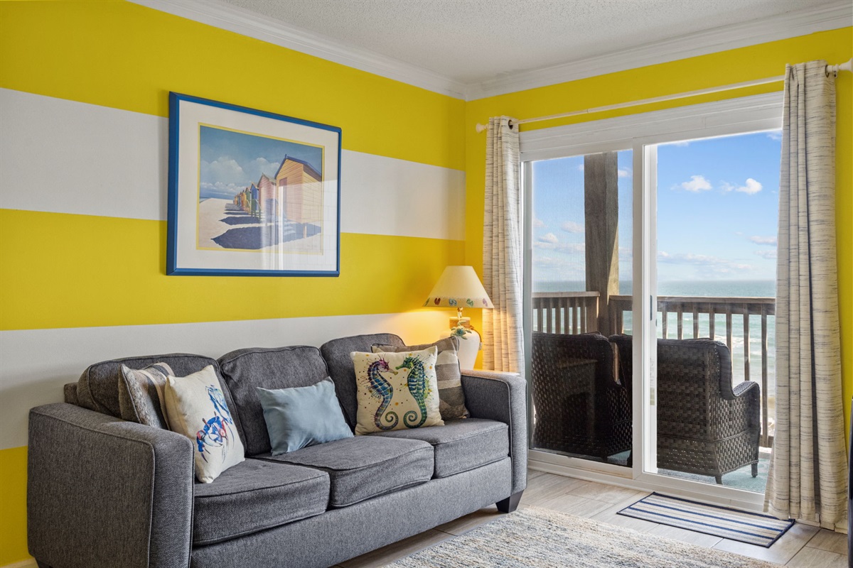 Bright coastal living space with comfortable seating and direct access to a private balcony overlooking the ocean