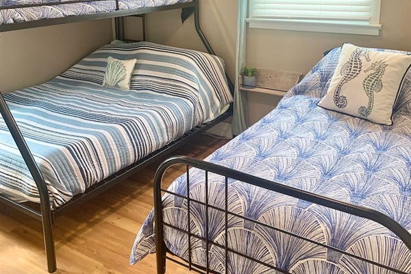 This cozy bunk room features a twin-over-full bunk bed and an additional twin bed, perfect for kids or extra guests. Coastal-themed bedding and seahorse pillows create a fun, nautical vibe for a relaxing stay.
