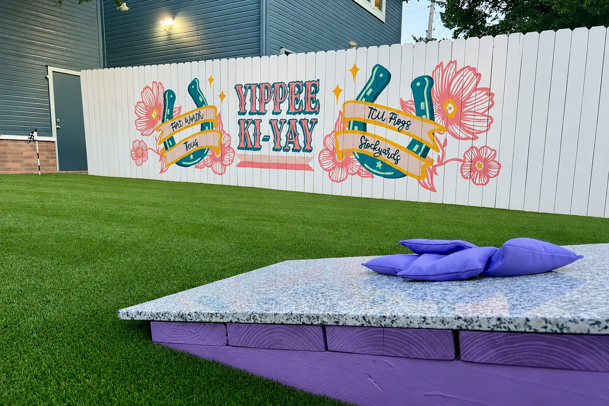 Cornhole and a custom mural add playful outdoor charm at The Style Studio, a Fort Worth vacation rental.

