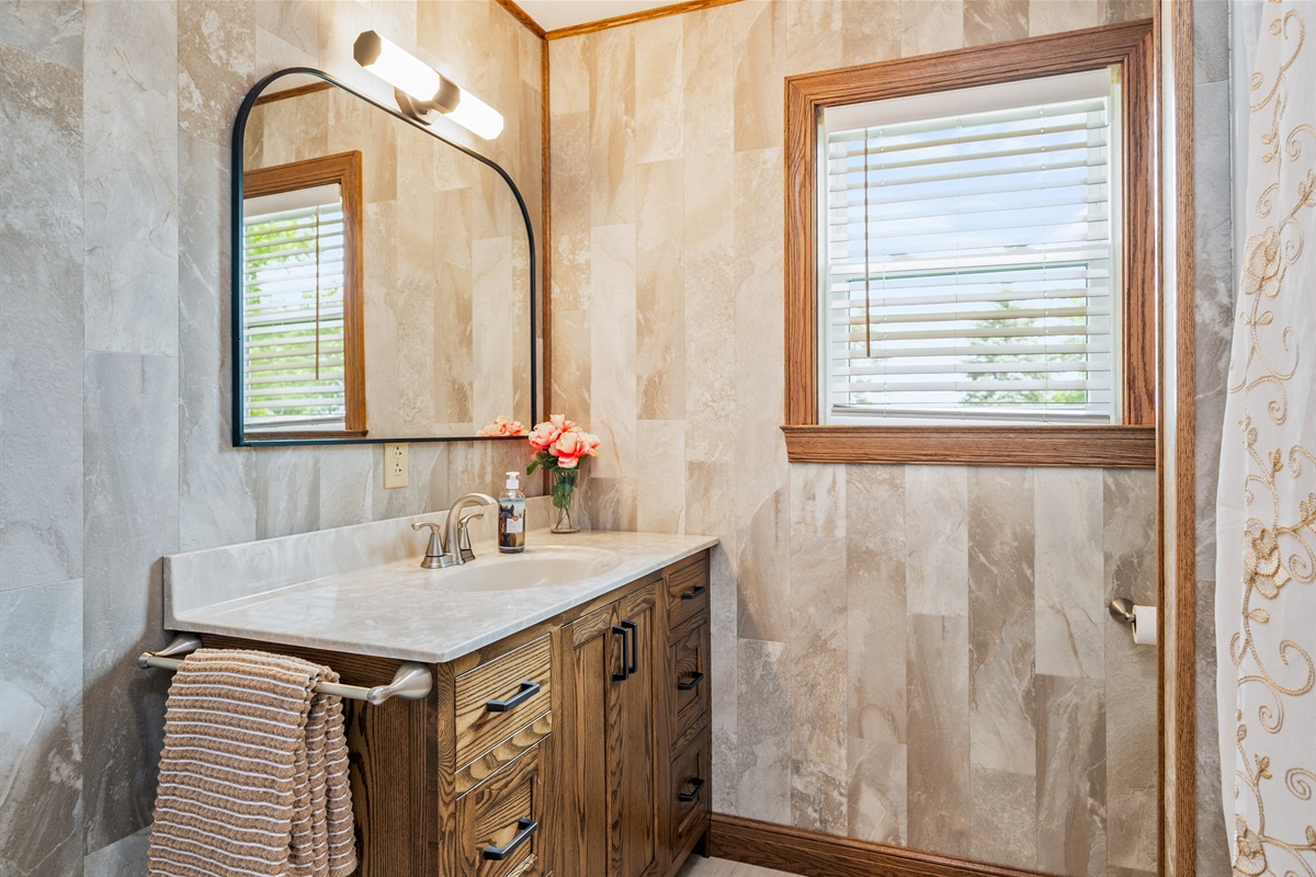 Clean and contemporary vanity setup with a large mirror, warm wood cabinets, and soft lighting.
