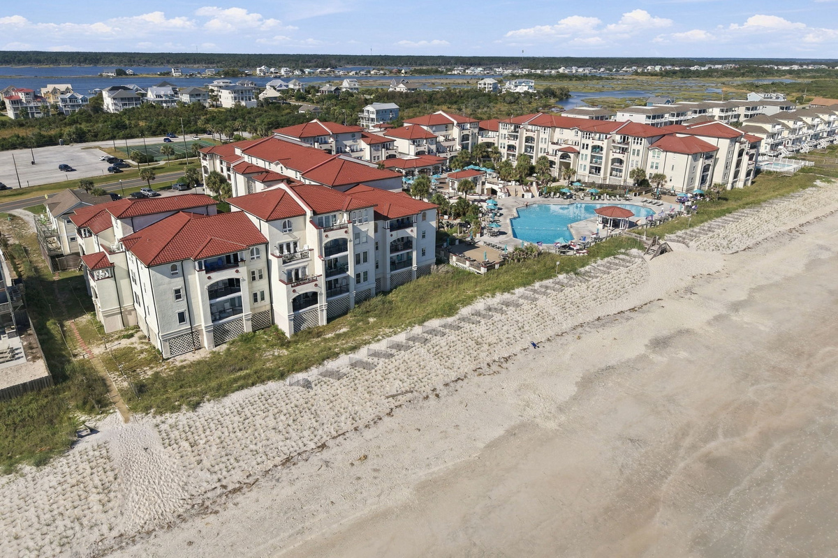 Oceanfront aerial overview showcasing the resort complex, terracotta roofs, central pool area, and direct dune-lined beach access.