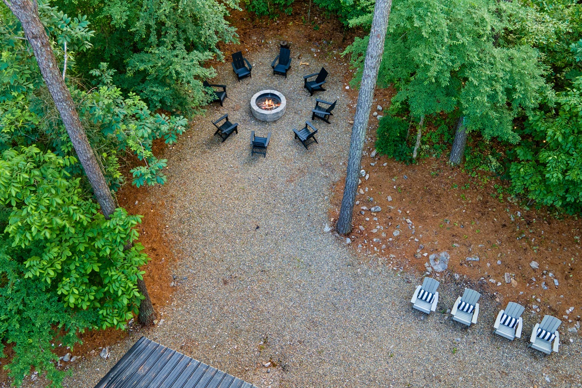 Aerial view of a cozy outdoor fire pit area with surrounding chairs nestled among tall trees.