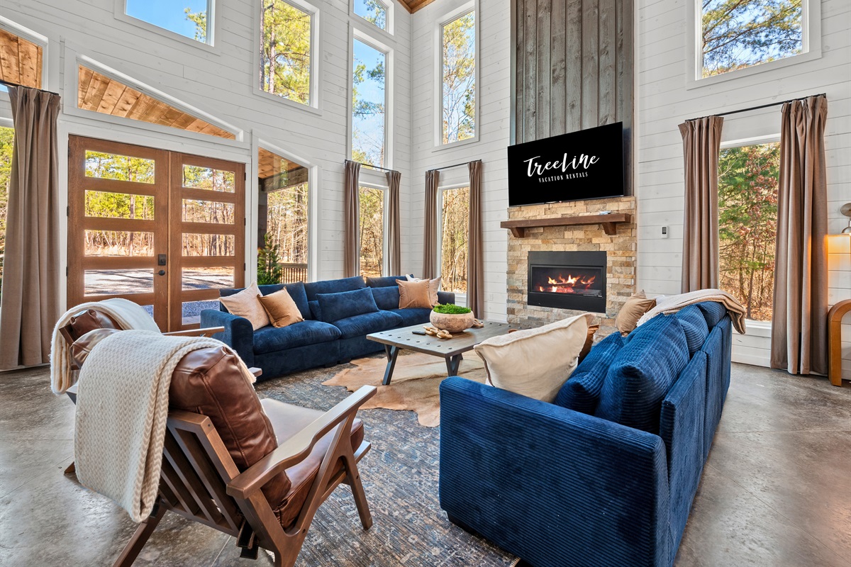 The open living space is designed for gathering, with a cozy fireplace, high ceilings, and oversized windows that bring the outdoors in.