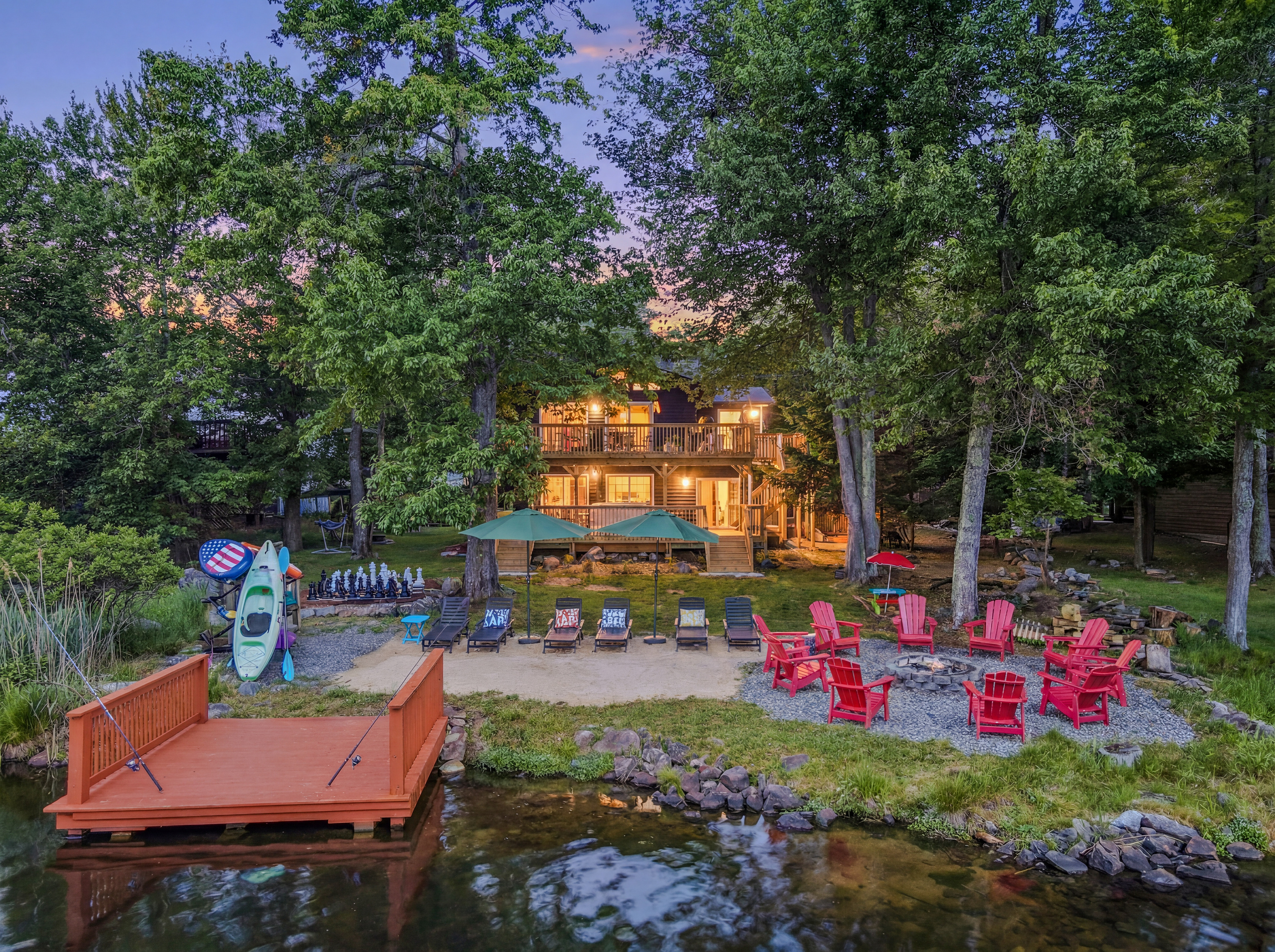 Full backyard view at dusk — dock, fire pit seating, lounge chairs, and the lake beyond