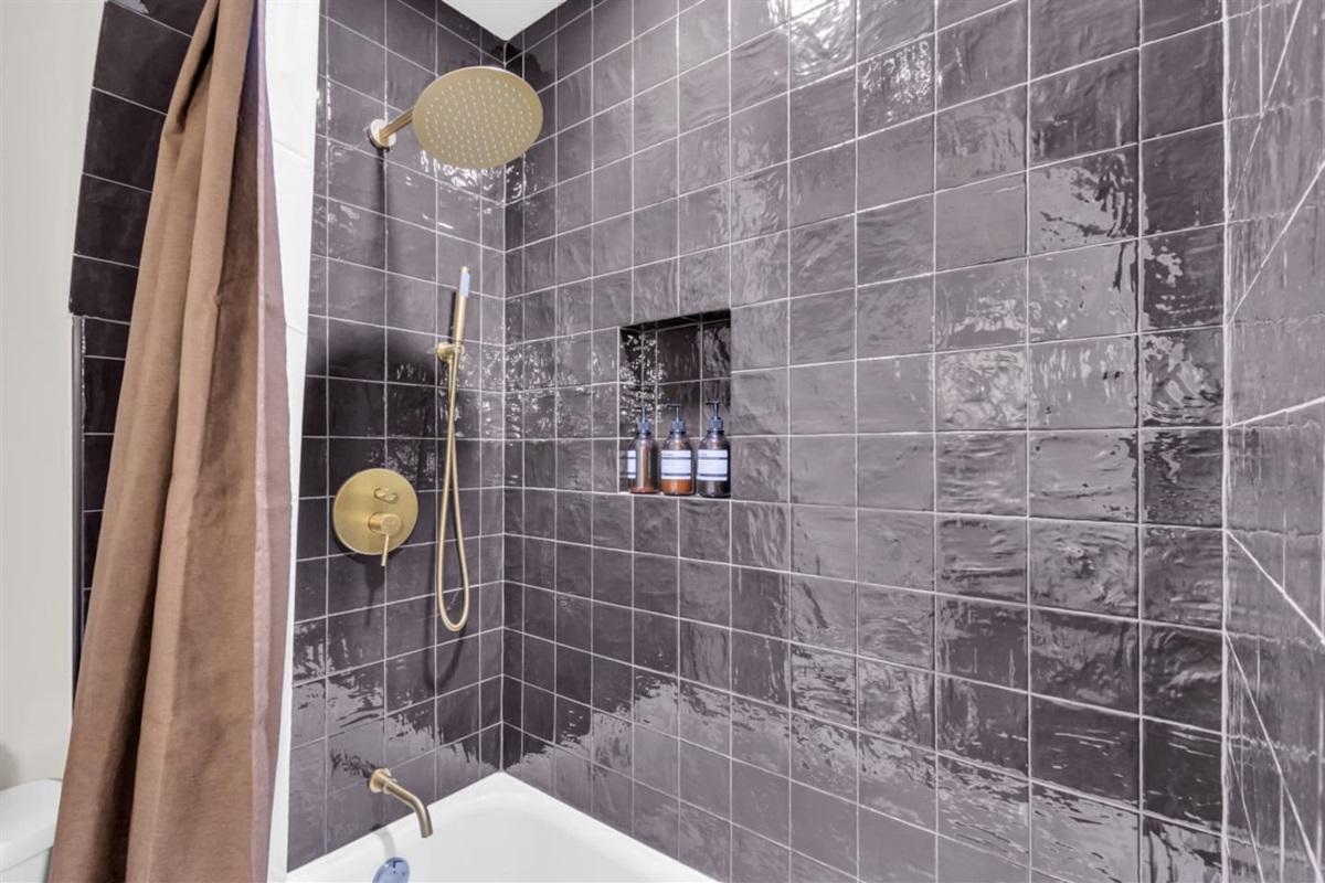Bathtub and shower combination featuring gorgeous tile work and fully stocked with essential bath amenities for a comfortable and stylish experience.