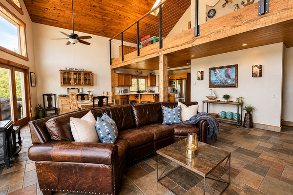 Spacious open-concept lakefront living area with soaring wood ceilings, comfortable seating, and an open layout connecting the living room, dining area, and fully equipped kitchen.
