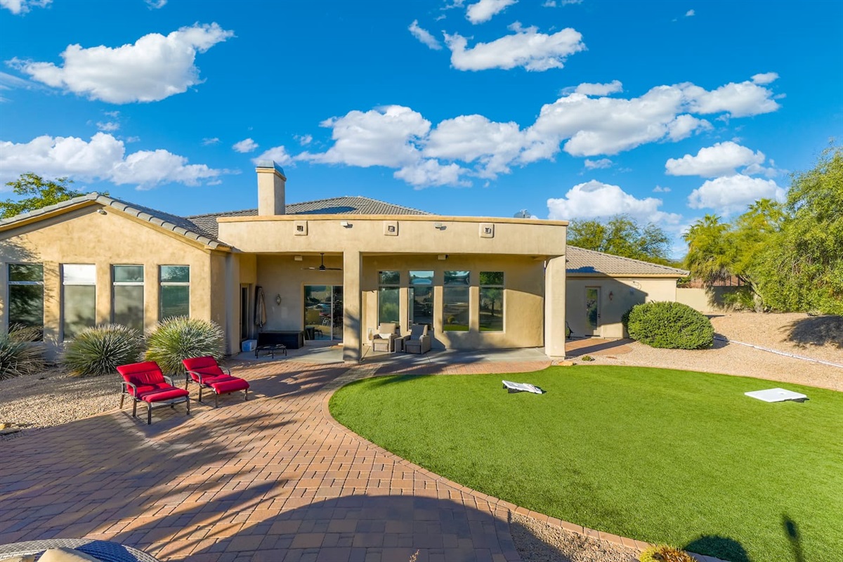 Wide backyard view showcasing the lush turf, curved paver patio, and comfortable outdoor lounging areas.