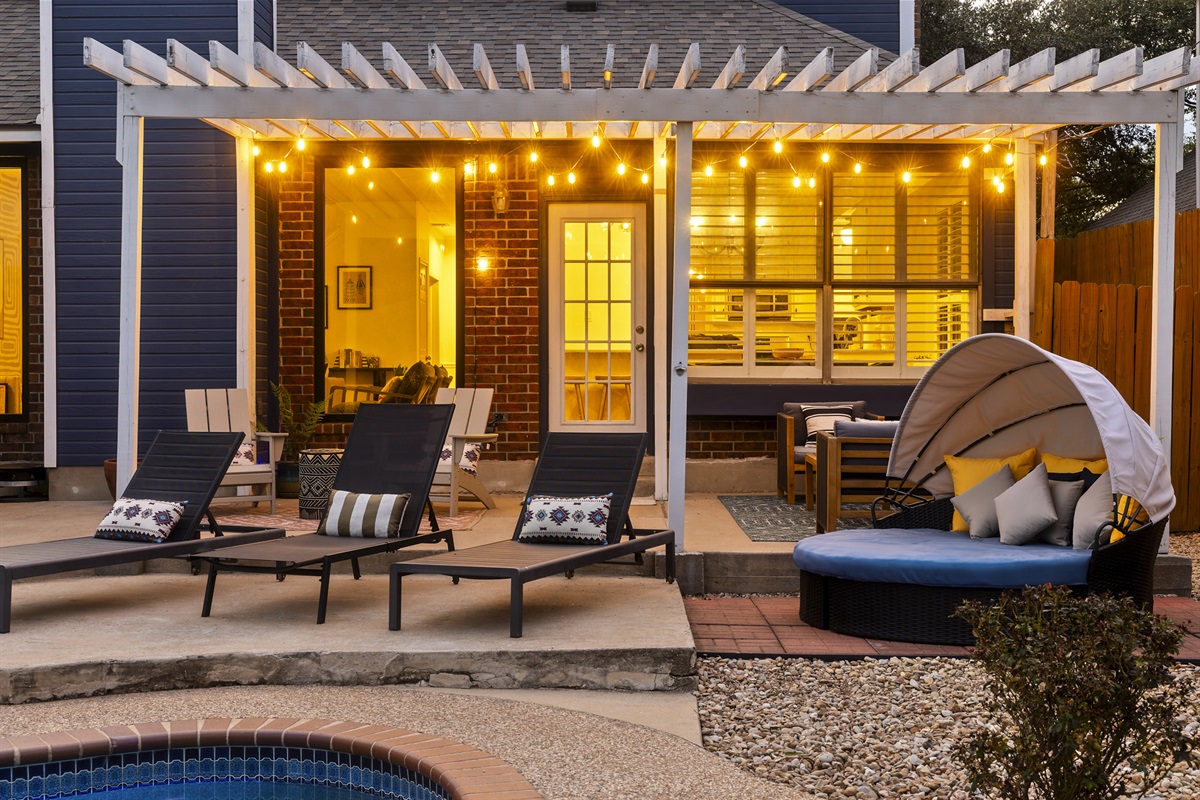 Relax in style under the pergola with chic lounge chairs and cozy seating. This inviting outdoor space, adorned with string lights, is perfect for unwinding by the pool or enjoying evening conversations