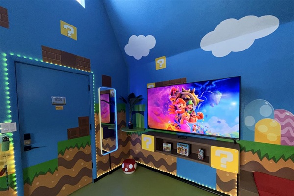 Vibrant blue walls with Super Mario murals, glowing question mark blocks, green pipes, and brick details surround the extra large 75" smart TV (+ Nintendo Switch system). The mirror lights up and plays music via Bluetooth, perfect for family fun!