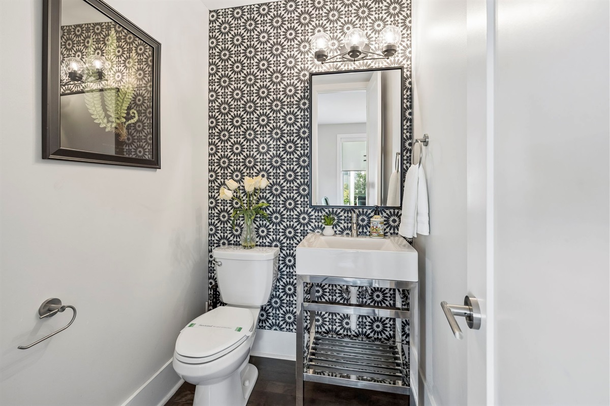 Eye catching black and white floral tile adds personality to this half bath - Sleek chrome vanity with open shelf and bold mirror elevate the modern vibe - Fresh florals, gold accent bin, and minimal d&eacute;cor create a polished guest space