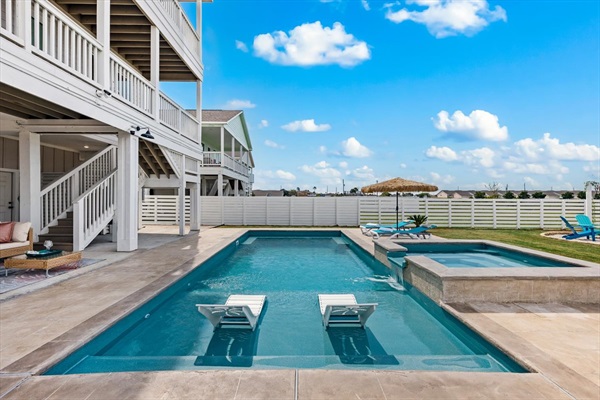 "Step into private backyard oasis featuring a sparkling pool and hot spa surrounded by modern walkways, mini golf, fire pit, and resort style vibes perfect for relaxing after a day at the beach".
