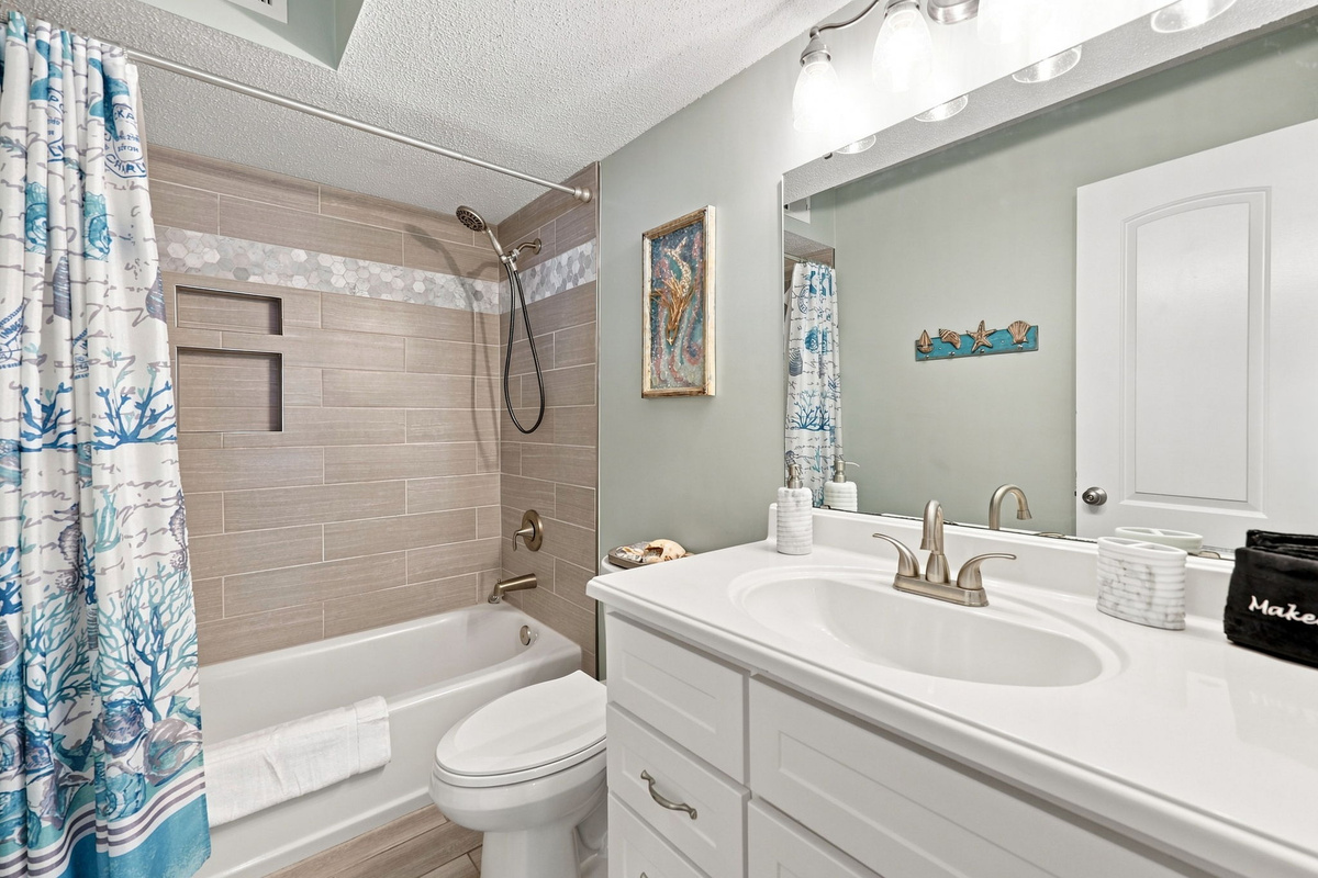 Clean and updated bathroom featuring a full bathtub with a decorative shower curtain, tile walls, and a large vanity mirror.