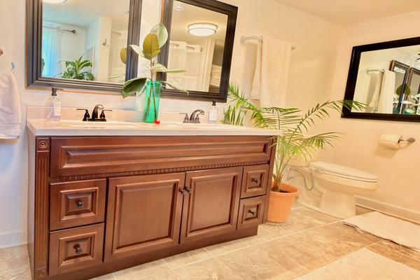 Spa bath with double vanity, bidet commode, tile floor, and organic cotton towels. Features a shower-tub combo (visible in mirror) and living plants.