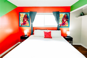 Modern Oasis: King Bed in Crisp White with a Hint of Orange, Set against Bluish-Green Curtains and Harmonious Green-and-Orange Walls. Natural Light and Entertainment Await 🍊🌿📺