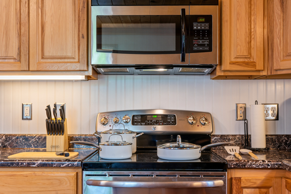 Cook effortlessly utilizing the stocked ceramic-coated nonstick pots and pans set arranged on the glass cooktop. The station features an electric range, an over-the-range microwave, a wood cutting board, and a Farberware knife block set.