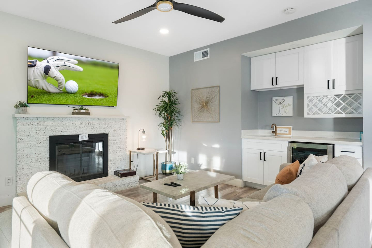 Light-filled living room with fireplace, bar, smart TV, and dual seating areas.
