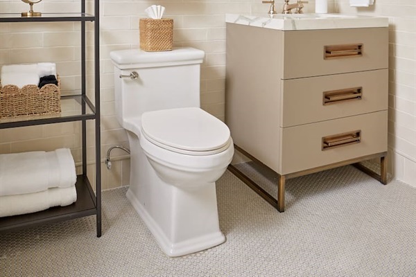 The spacious first-floor ensuite bathroom features classic penny-round tile flooring, a custom vanity with quartz countertops, designer lighting, and a large shower with elegant Kohler fixtures for a luxurious touch.