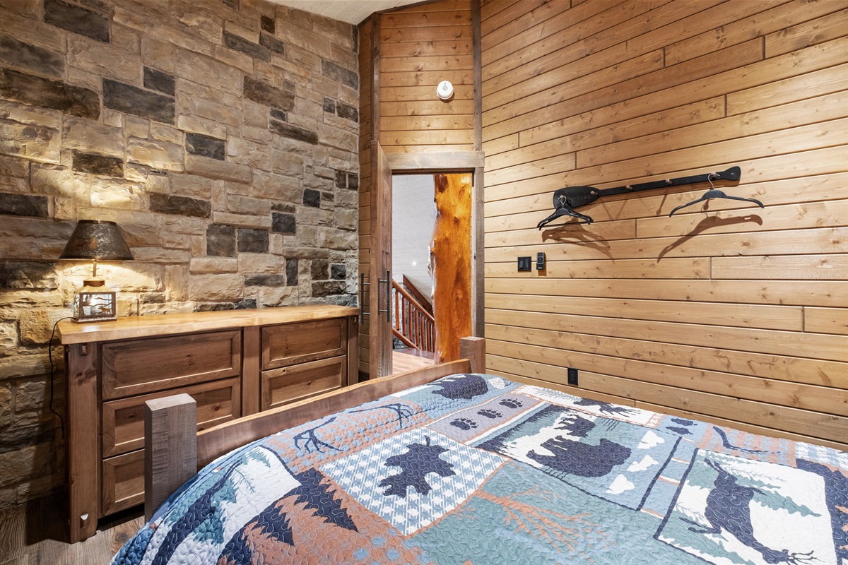 Rustic queen bedroom featuring beautiful log construction, a stone accent wall, and soft cabin lighting for a true lodge-style sleep experience.