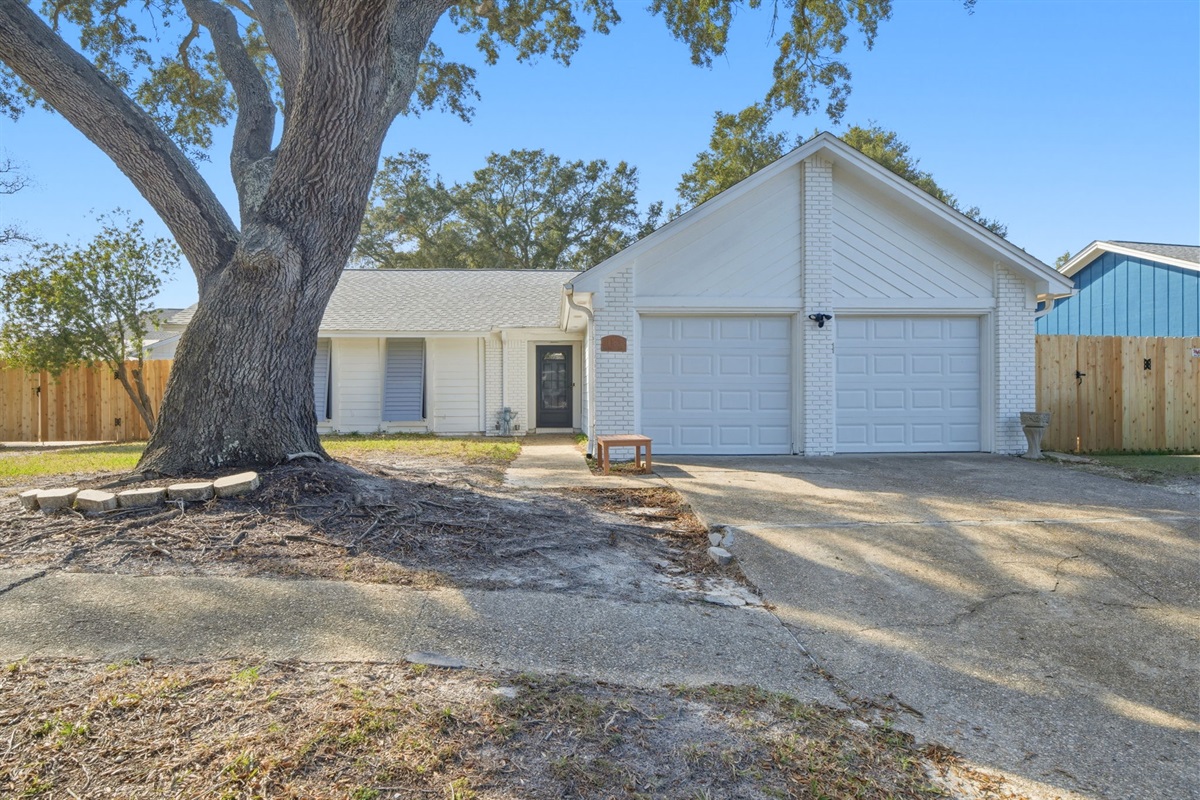 The front of the home showcases a welcoming exterior with a large shade tree, spacious driveway, and attached two-car garage. The simple landscaping and peaceful neighborhood setting make this property feel both inviting and private.