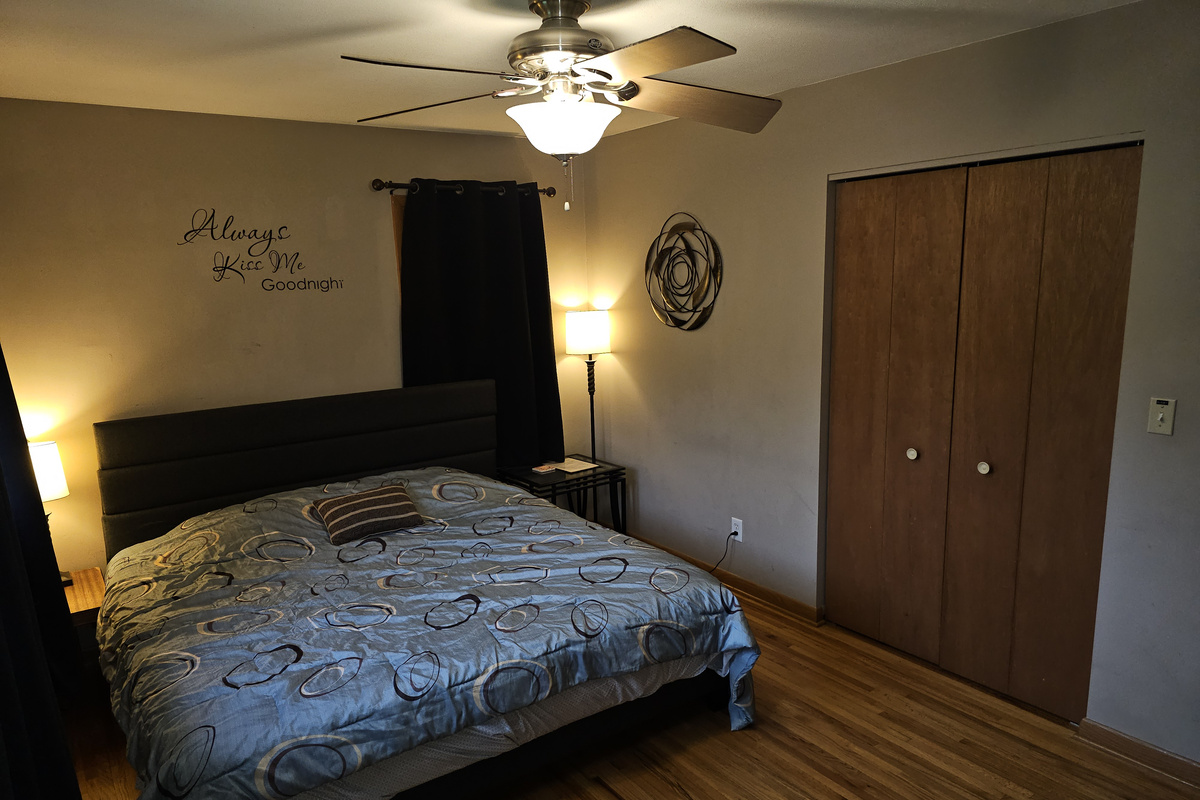 Master bedroom on the main floor with king bed, ceiling fan, alarm clock and a smart tv.
