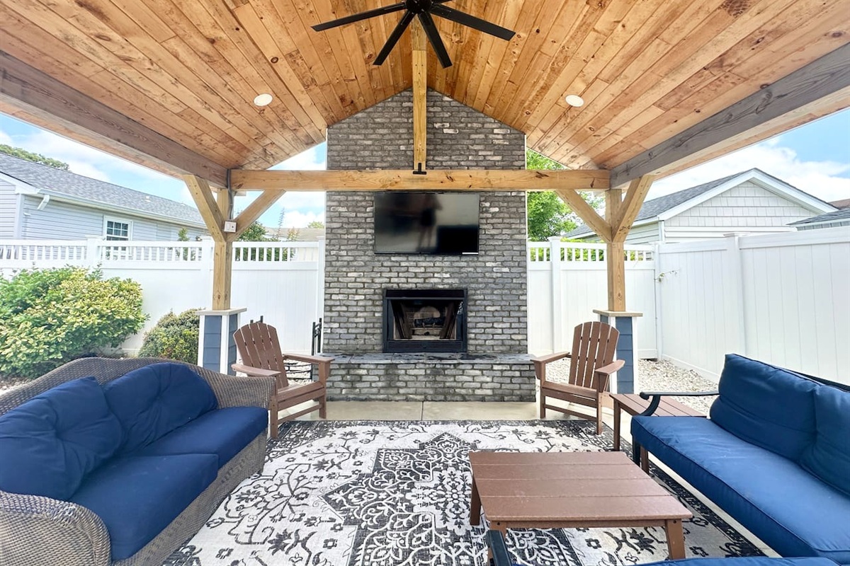 Unwind in luxury under this vaulted wood ceiling. The covered lounge features a grand stone fireplace and outdoor TV, offering a cozy, stylish escape for your next vacation.