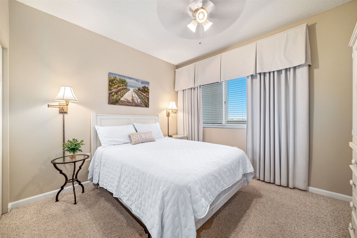 This well-appointed bedroom features a queen -size bed with a decorative headboard, crisp white bedding, matching nightstands with lamps, and tile flooring for easy maintenance.