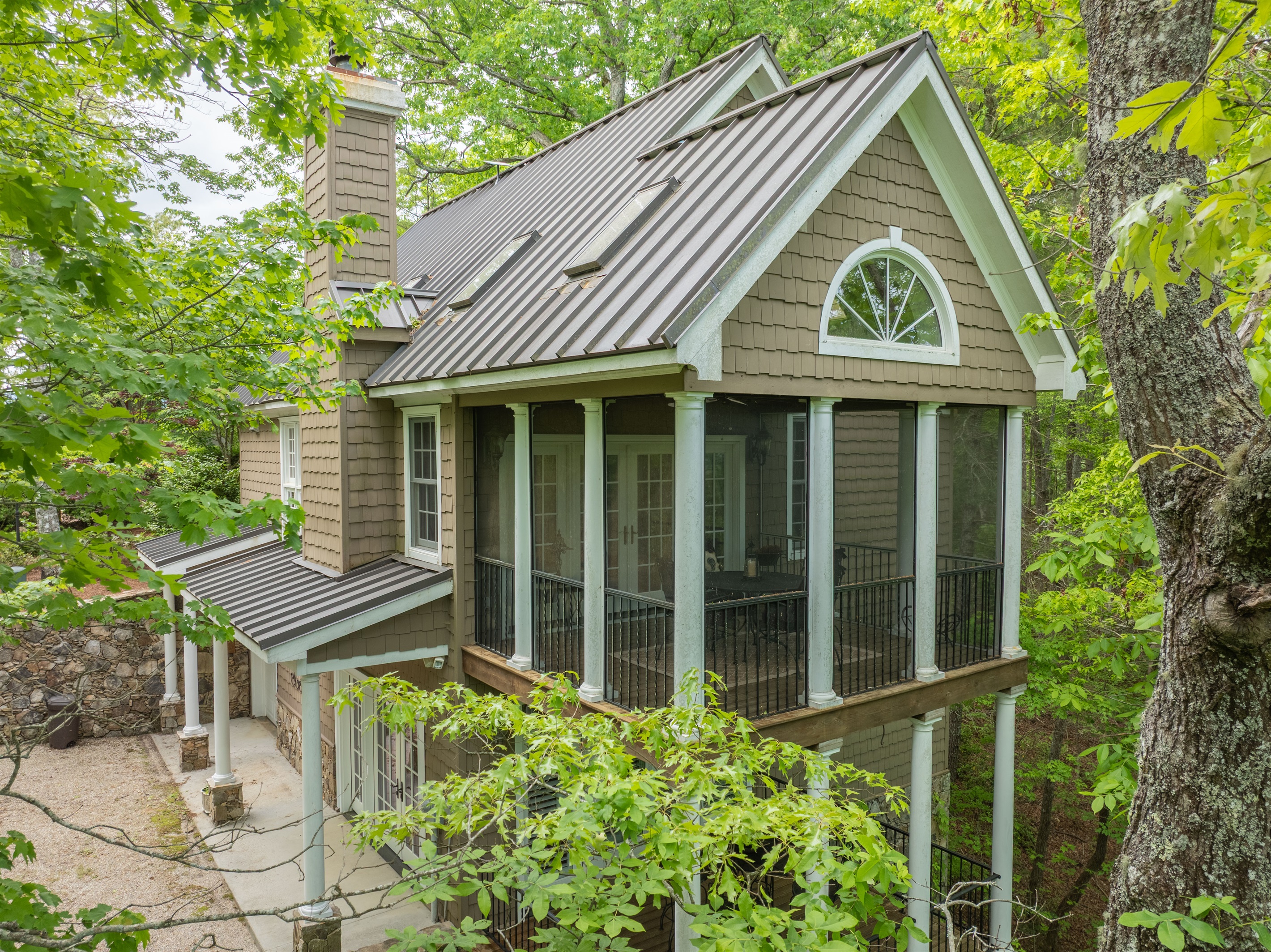 Cheoah Cottage features striking architecture, a metal roof, and a beautiful screened porch nestled among the trees.