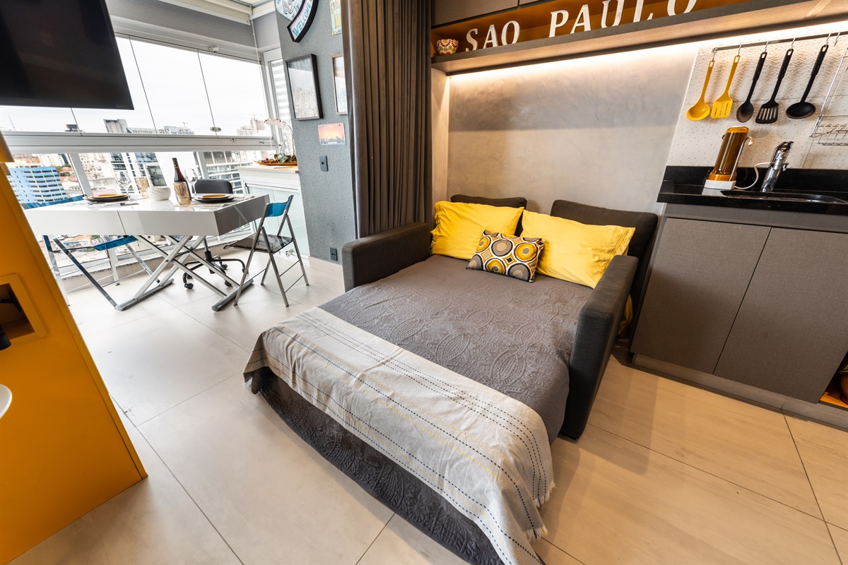 Sala de estar versátil com sofá-cama e vista para a varanda, combinando conforto e praticidade