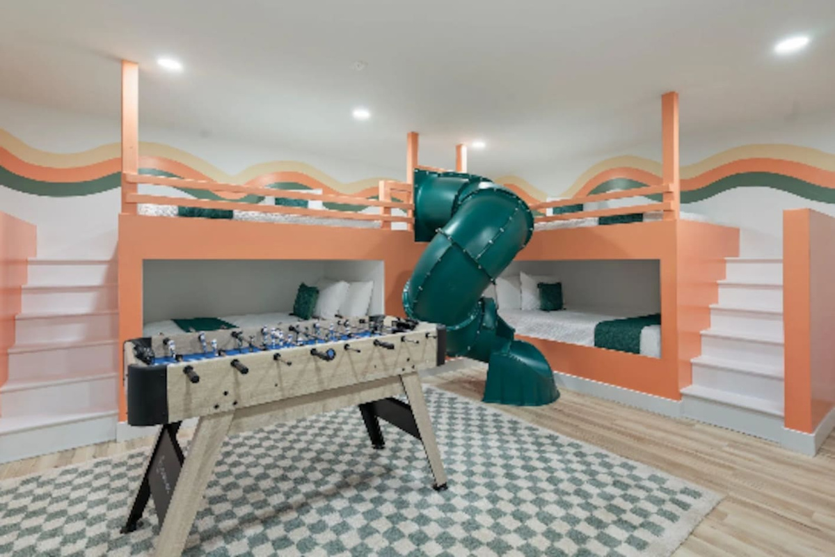 This isn't just a bedroom, it's a full-on kids' playground. Twin bunks tucked into a sunset-striped mural, a foosball table for rainy afternoons, and a slide connecting the top bunk straight down to the floor. 