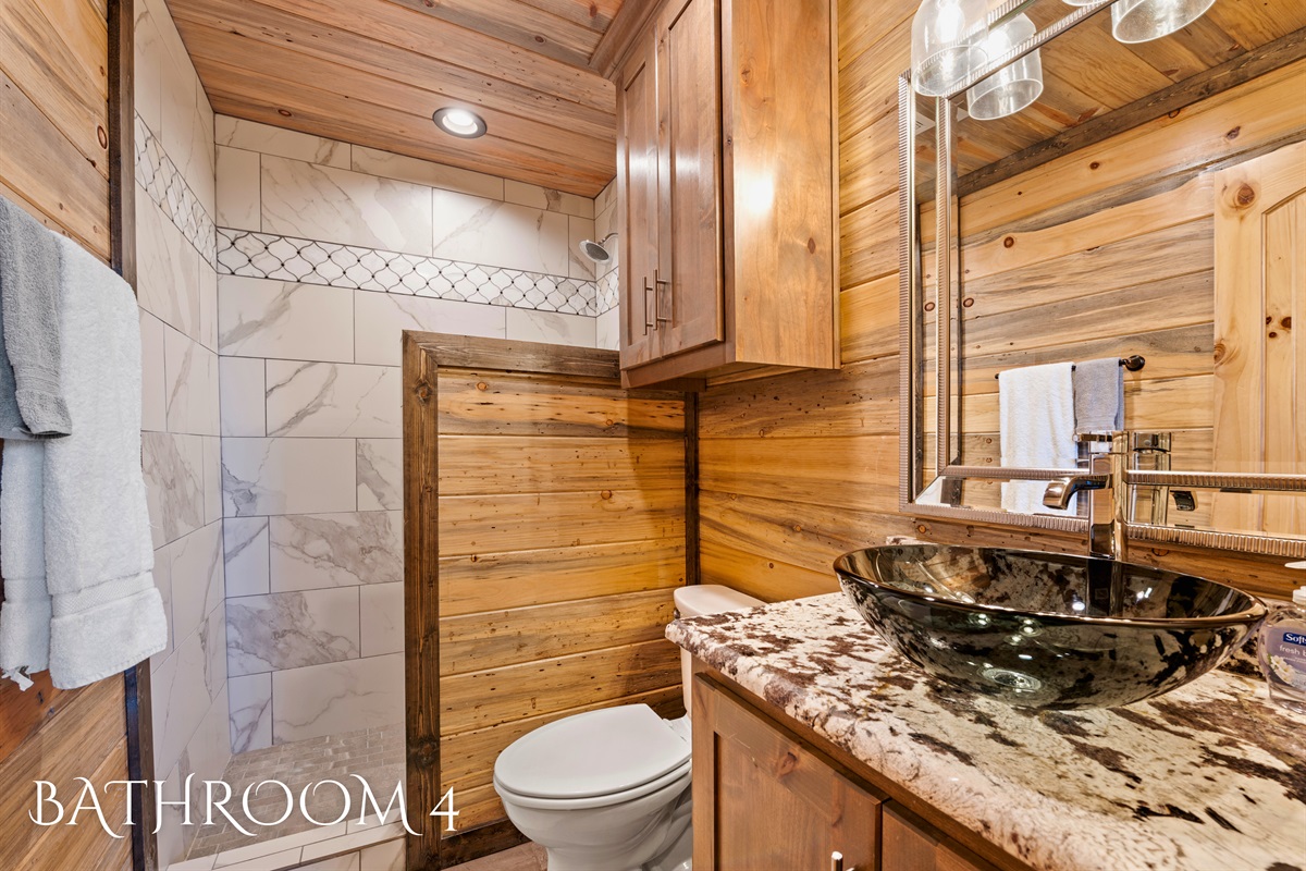 A stylish bathroom equipped with a wall shower, a wooden vanity with a unique vessel sink, and a harmonious blend of wood tones.