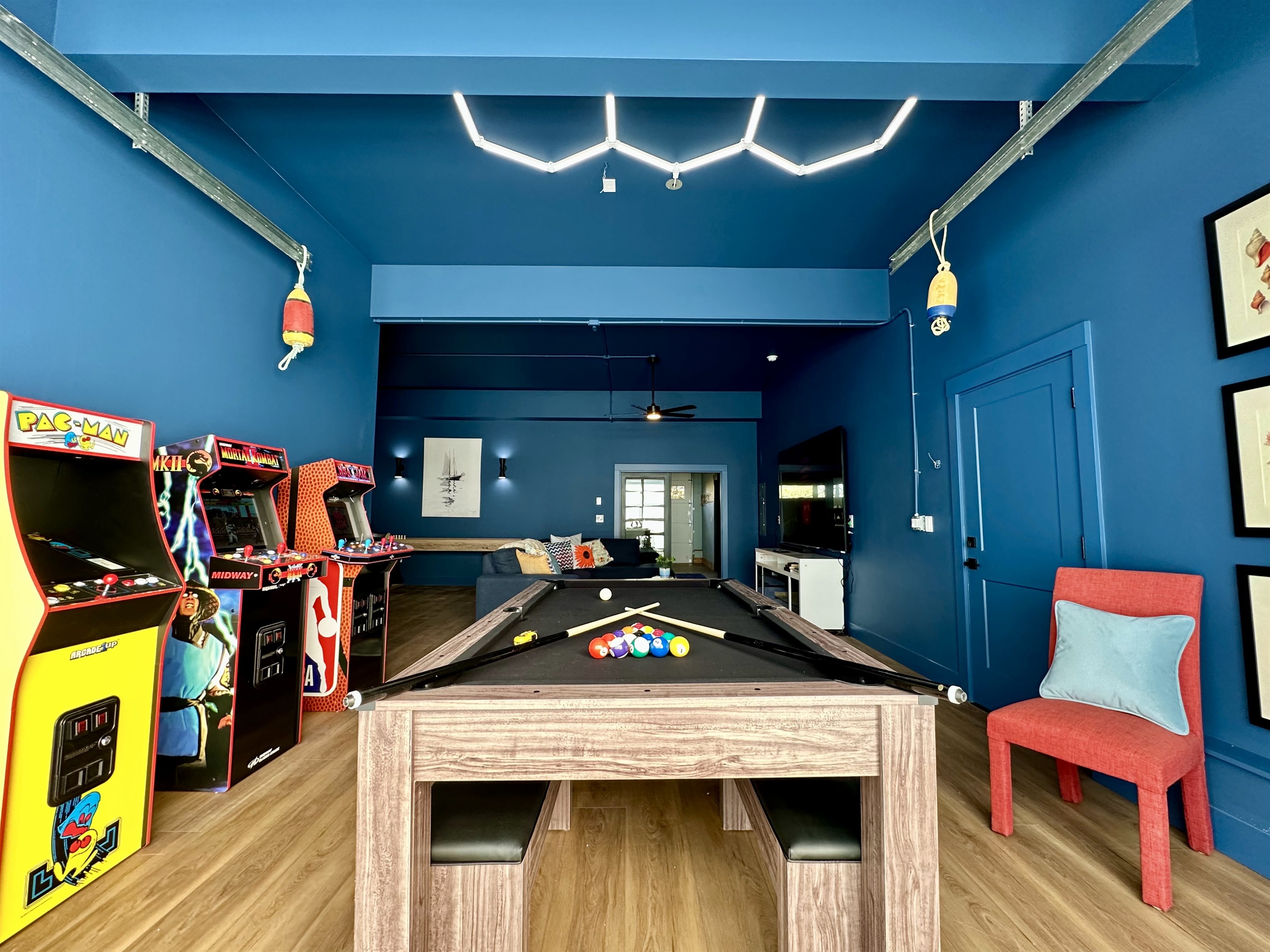 The full picture: arcade machines, pool table, sectional sofa, shuffleboard, poker table, and natural light pouring in from the open garage door. This isn't a room — it's a destination.