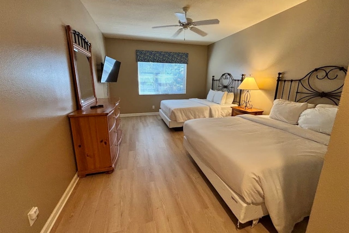 Spacious bedroom featuring two beds, ceiling fan, dresser storage, and a bright, relaxing layout.