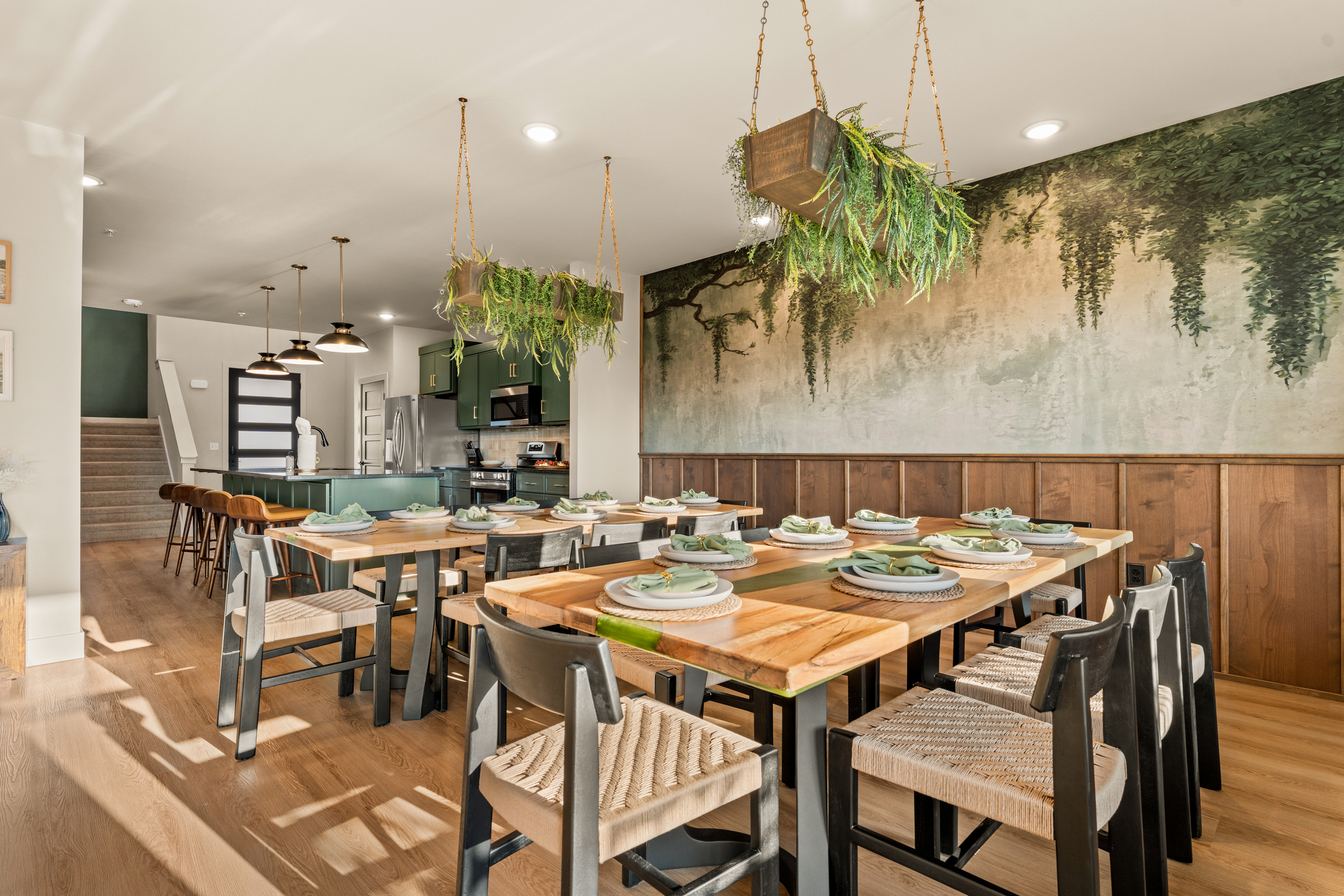 Gather around the beautifully styled dining space, where warm wood tones, lush hanging greenery, and a striking botanical mural create an inviting, nature-inspired setting for memorable meals together.
