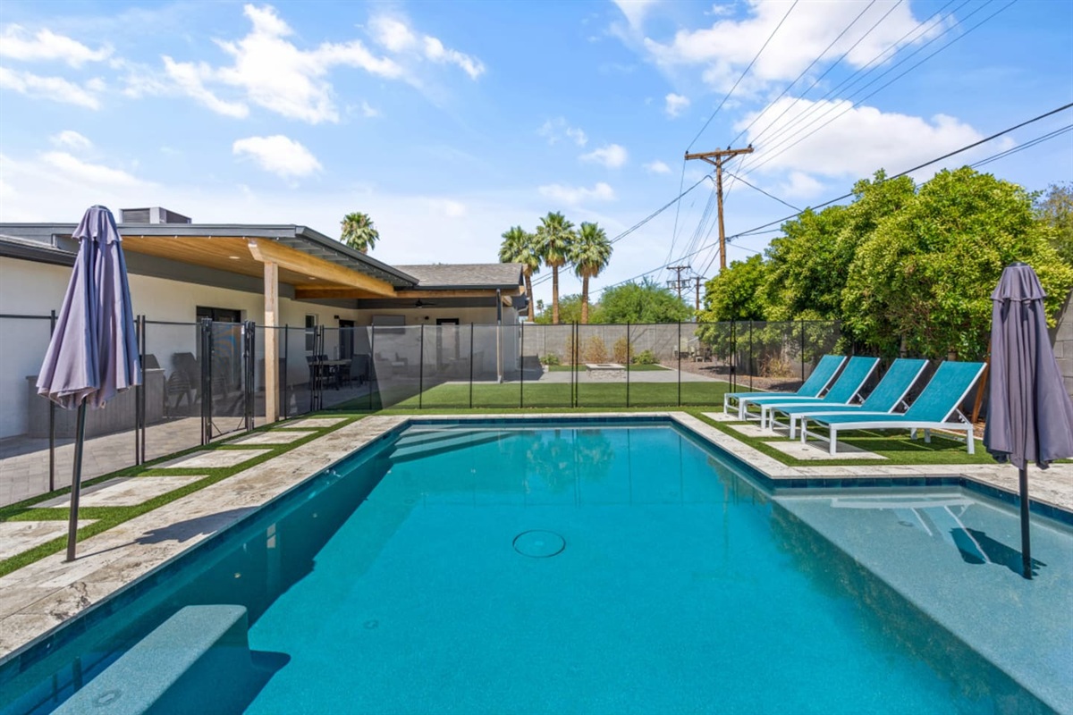 Private backyard pool with safety fence, lounge chairs, umbrella shade, fire pit seating, and a bright outdoor space 