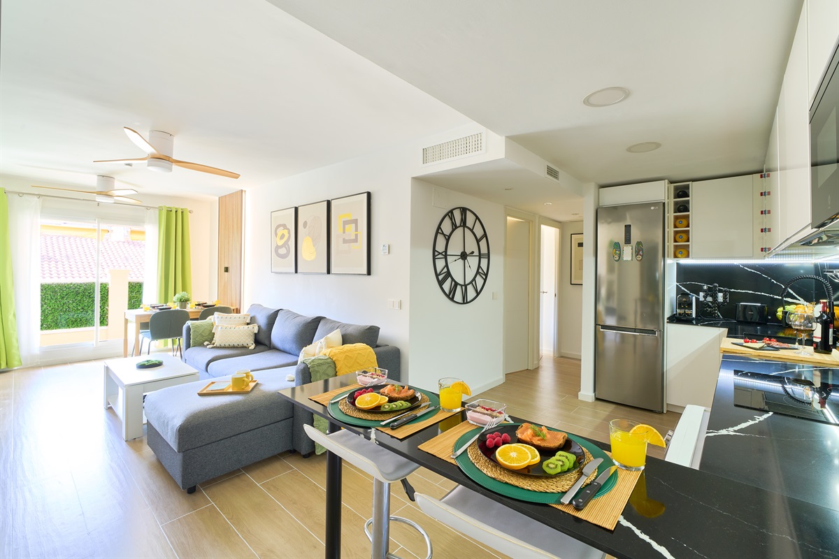 Stylish open-plan living room with a modern kitchen, smart TV, and natural light throughout — ideal for relaxing or sharing a glass of wine after a day by the beach.