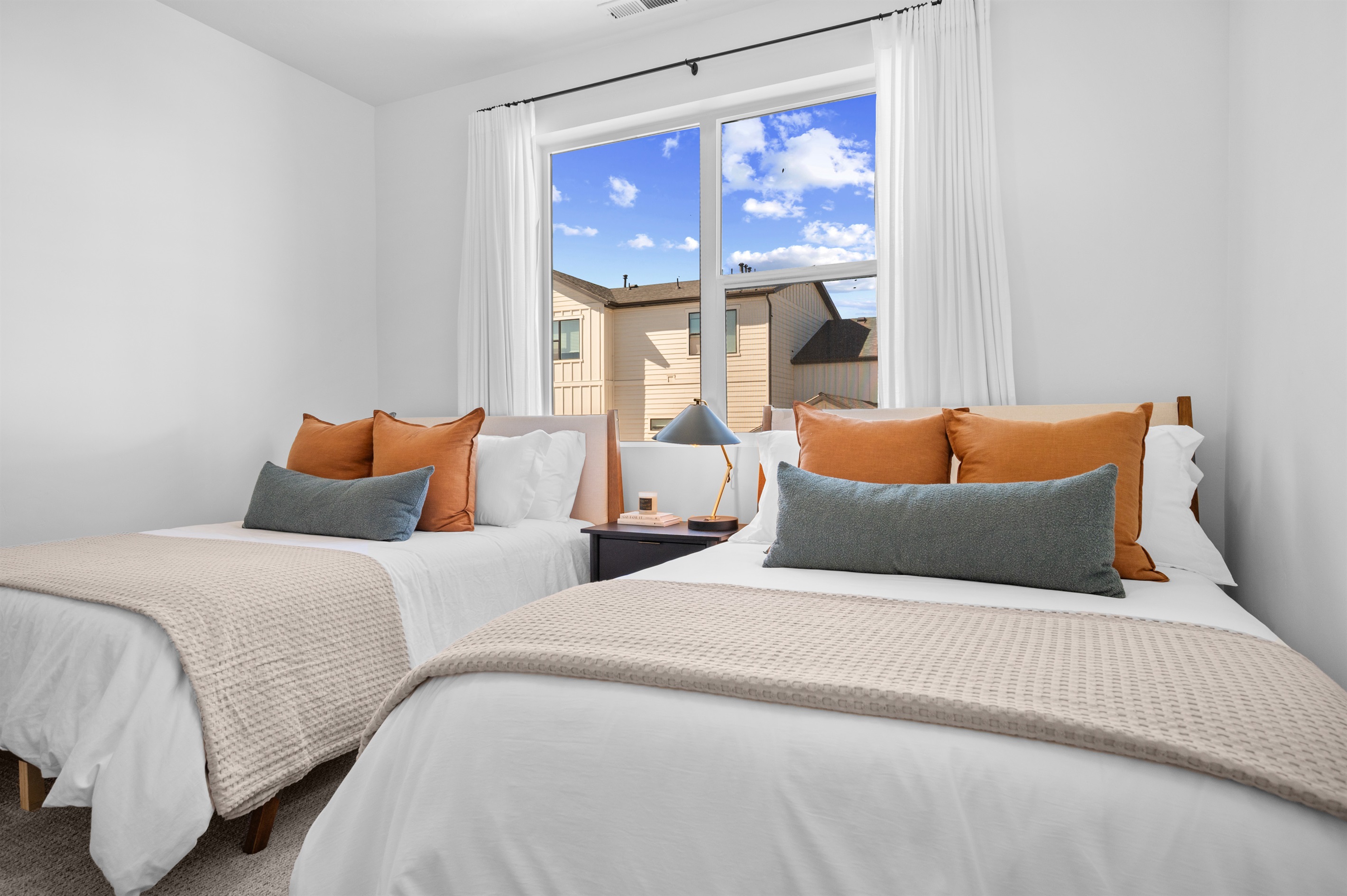 Bright guest room featuring twin full beds, warm accent pillows, and natural light.