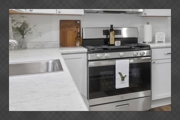 Fully equipped kitchen with white cabinetry, stainless steel appliances, and spacious marble-look countertops.