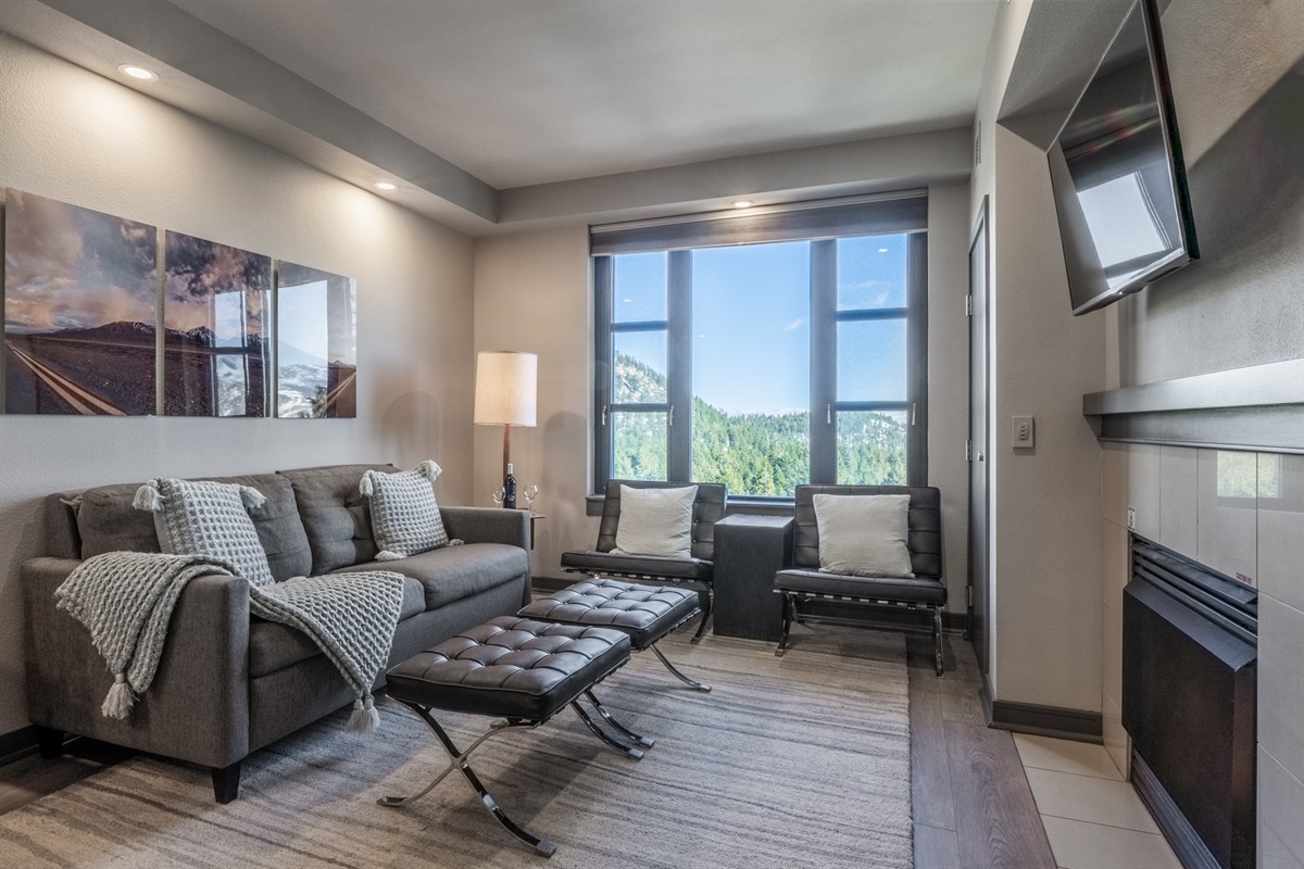 A cozy living area with sofa, ottomans, fireplace, and TV is paired with modern local photography and large windows that bring the outside in.