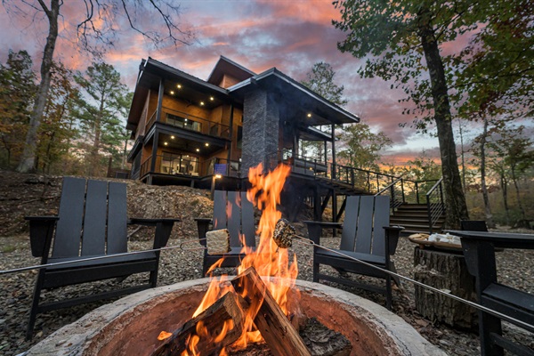 A perfect Broken Bow night: crackling fire, forest surroundings, and a beautifully lit cabin just behind you