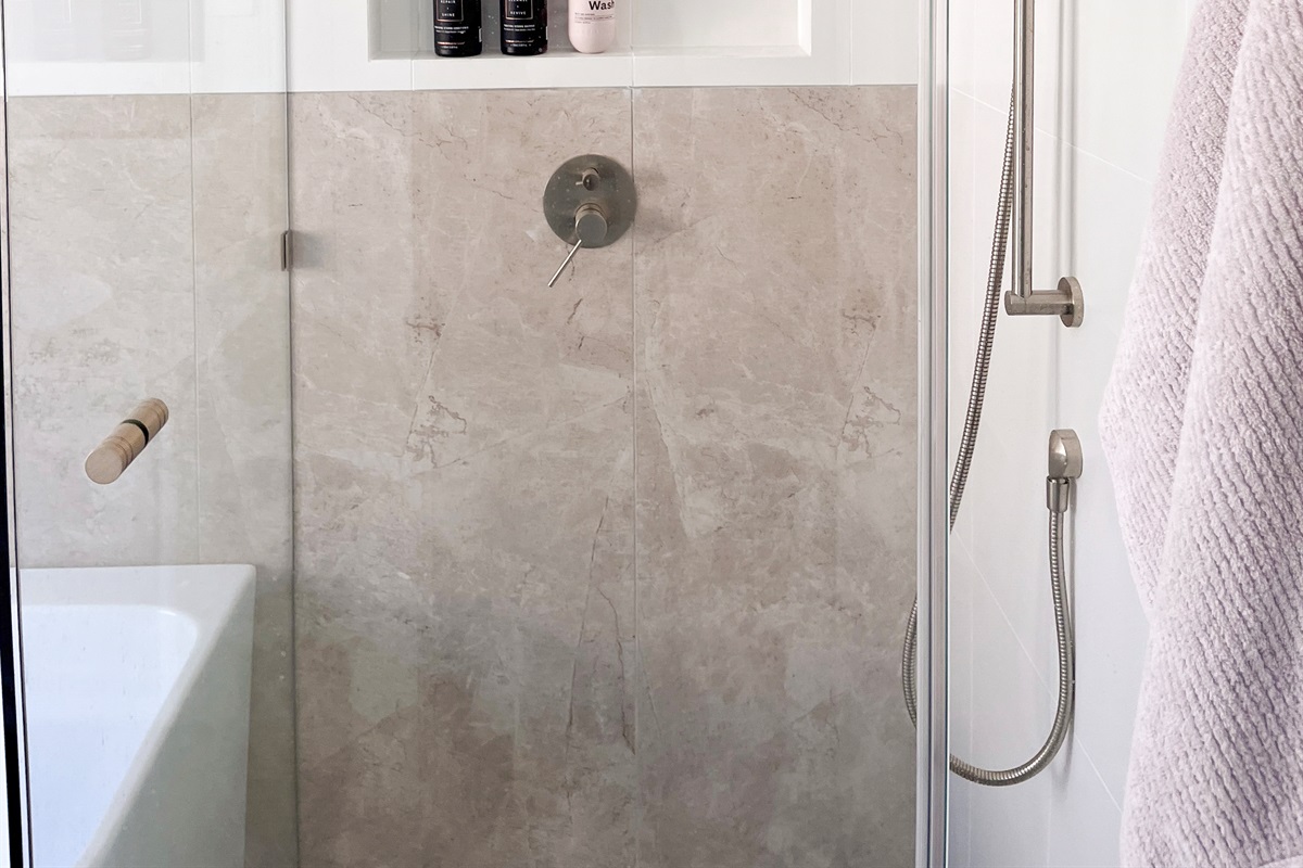 This bathroom combines a deep bathtub, walk-in shower, toilet and vanity in one practical space with neutral tiling.