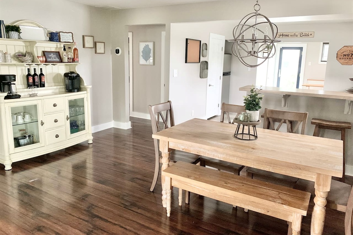 This charming dining area features a farmhouse table with bench seating and a unique orbital chandelier. A white hutch serves as a coffee and wine station, making it easy to enjoy a beverage before heading to the shore.