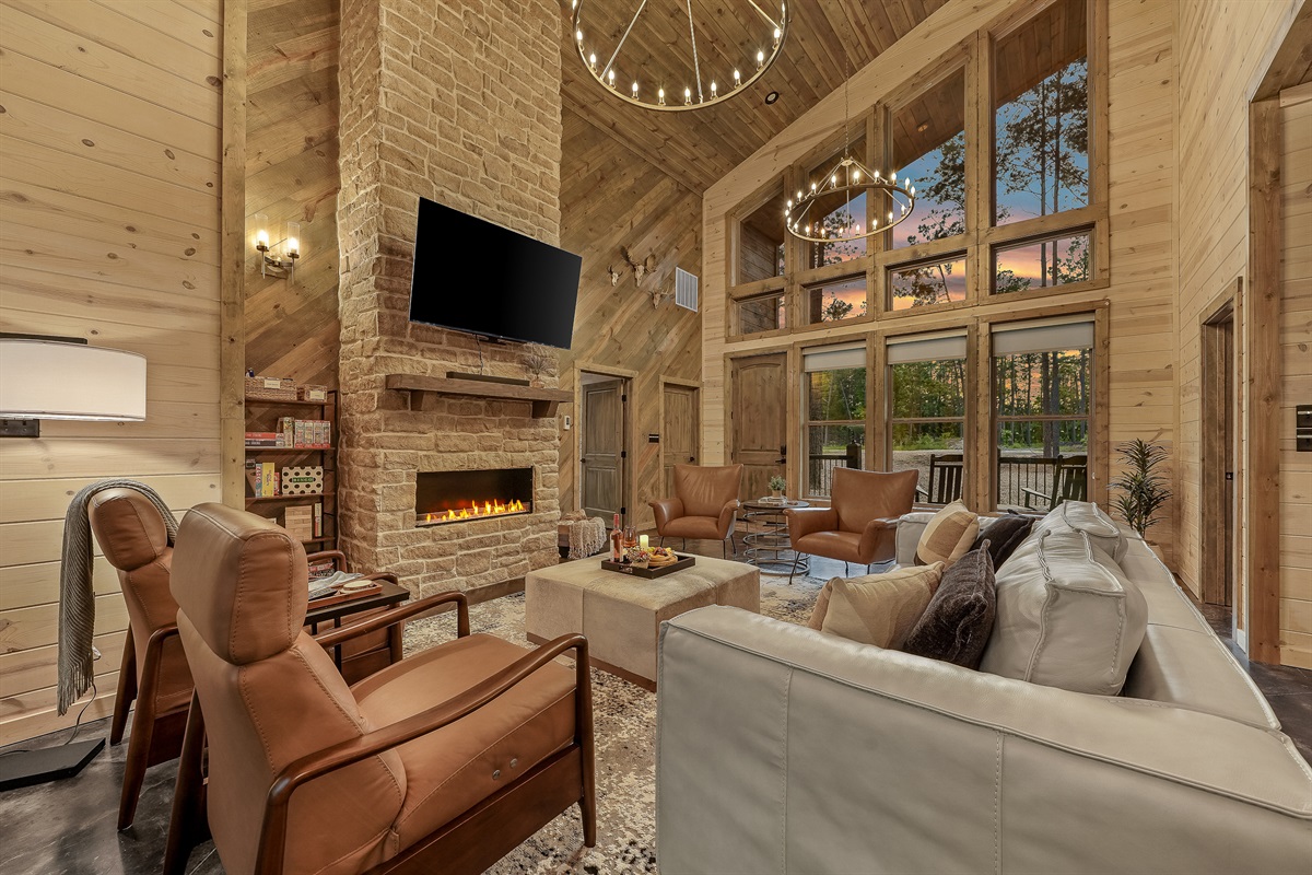 Relax in comfort and style in this inviting living room, featuring a leather sofa, two recliners, and cozy lounge chairs. Floor-to-ceiling views bring the forest indoors, while roller shades offer privacy and ambiance when you want it.