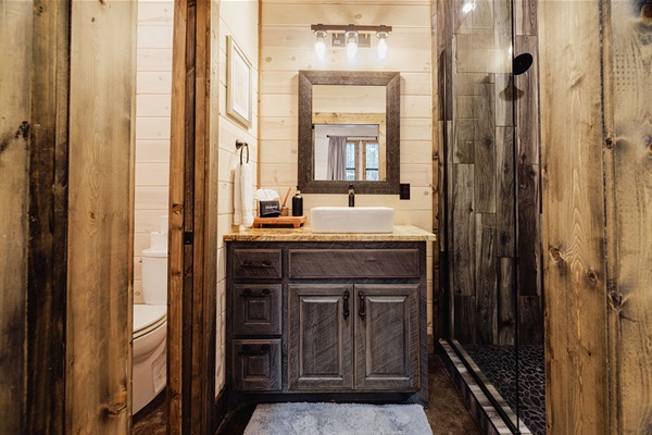 Cozy rustic bathroom with a dark wood vanity, vessel sink, large framed mirror, and warm lighting. A stylish mix of farmhouse and modern design in a luxury cabin.