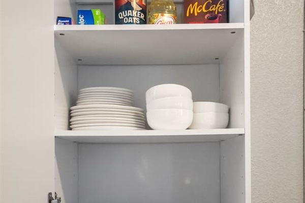 View of a well-organized cabinet stocked with dinnerware, silverware, pots and pans, and cutting boards, providing all the essentials for cooking and dining.