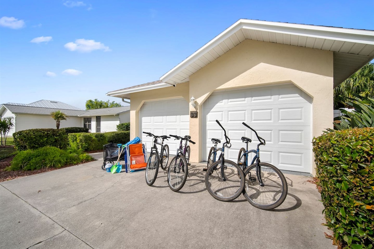 4 bikes and a beach cart with some sand toys and umbrella, and beach chairs