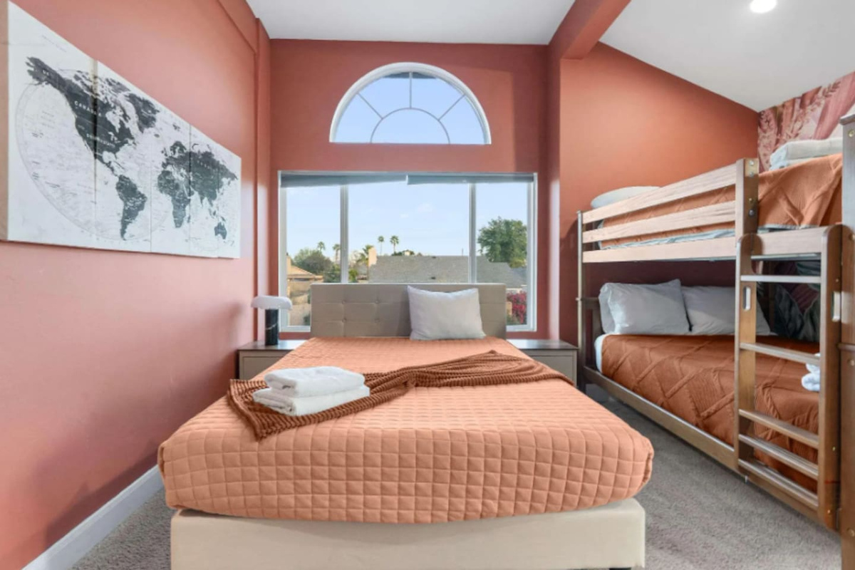 Bright guest bedroom with queen bed, bunk beds, arched windows, and views.
