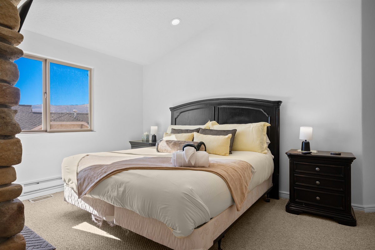 Cozy bedroom featuring a queen bed, neutral tones, and serene mountain views through large windows.