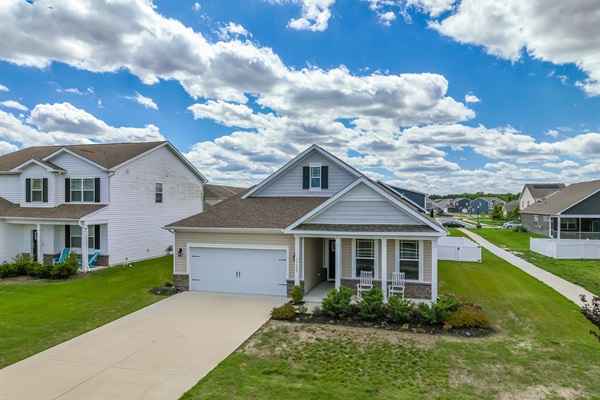 Approach via a smooth concrete driveway leading to a two-car garage, accented by manicured beds and welcoming rocking chairs on the covered front porch—your guests’ first glimpse of home comfort.