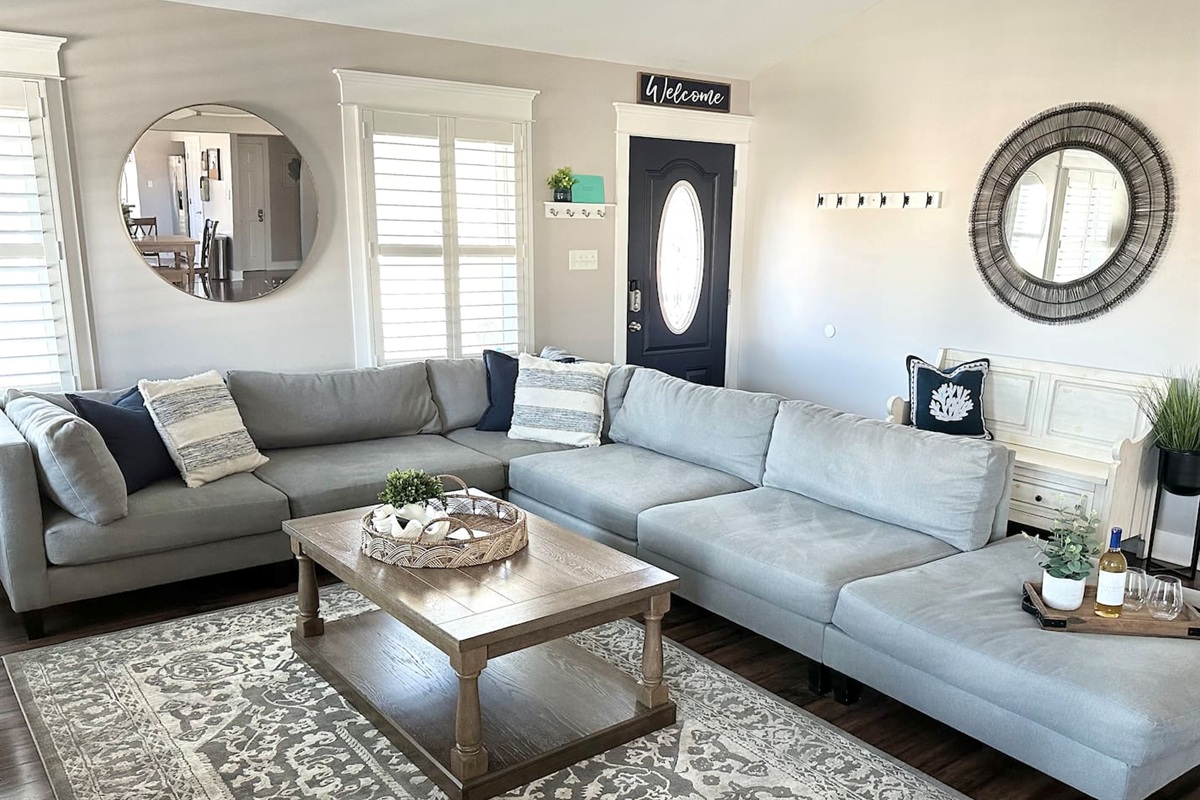This bright entry and living area features a large, comfortable sectional perfect for group gatherings. Elegant mirrors and coastal accents create an airy feel, making it a welcoming spot to kick off your shoes after a fun day at the beach.