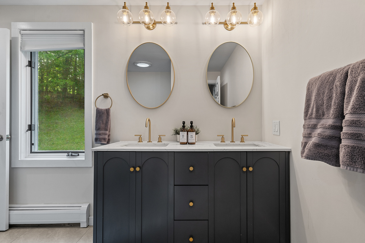 Shared bathroom with double vanity, navy cabinetry and brass fixtures